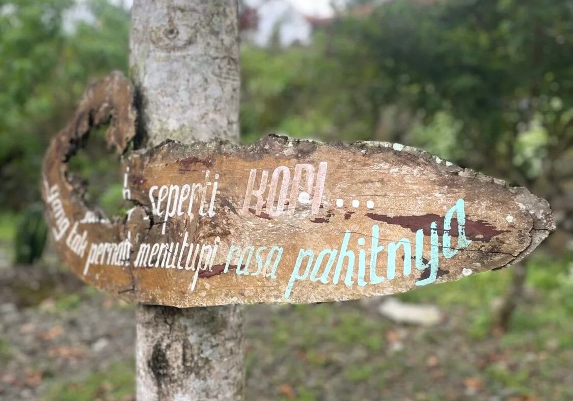 Rustic wooden sign with Indonesian text attached to a tree