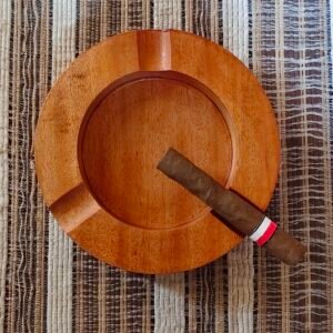 Cigar resting on wooden ashtray on striped surface.